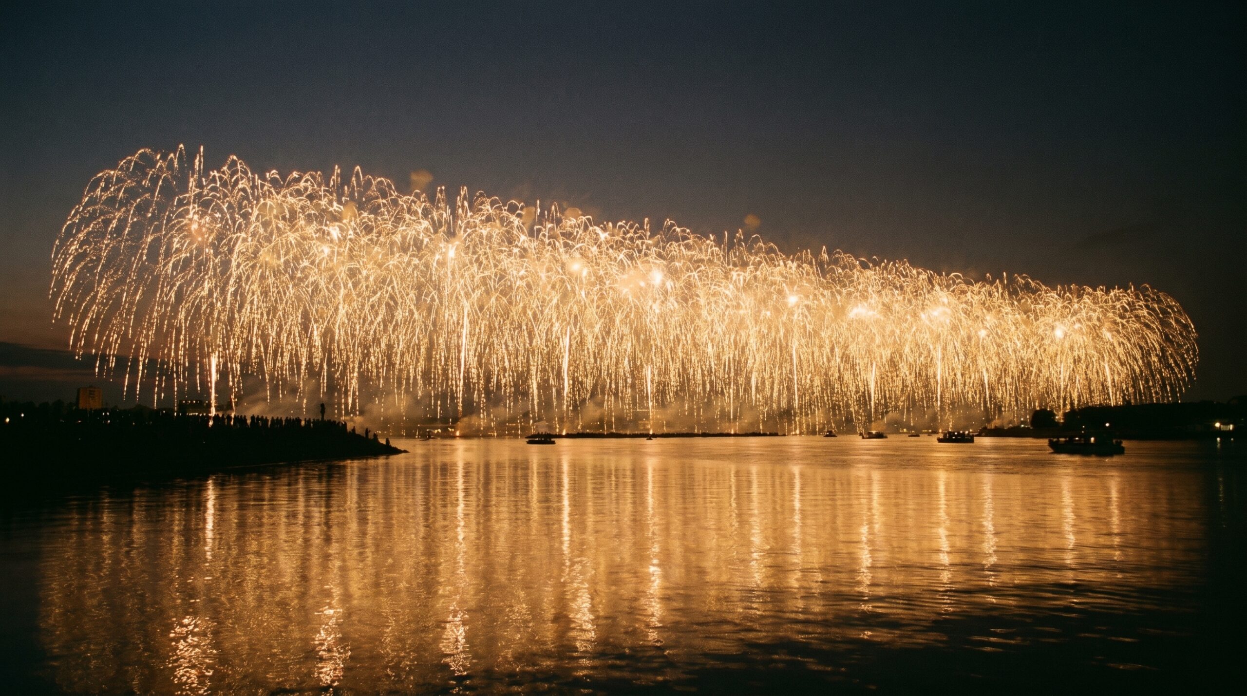 A wide curtain of golden fireworks over a river
