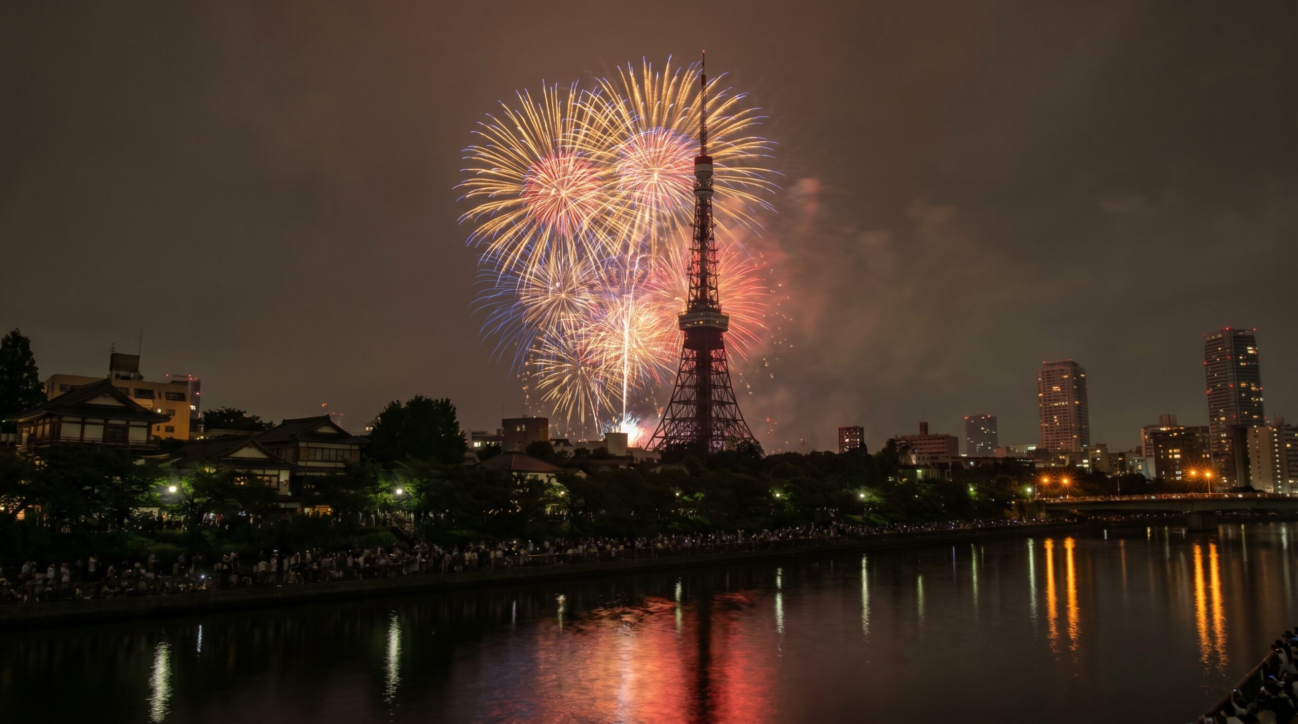 Fireworks over Tokyo with an illuminated tower and crowds