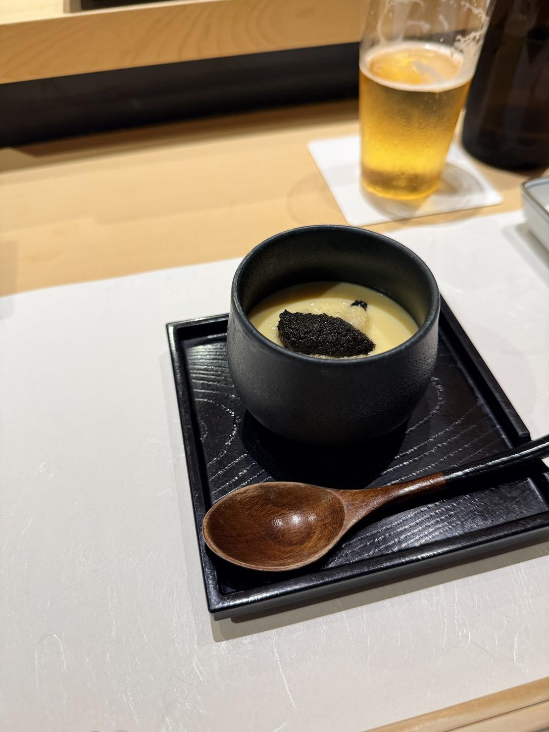 Savory dashi egg custard topped with black truffle in a black cup