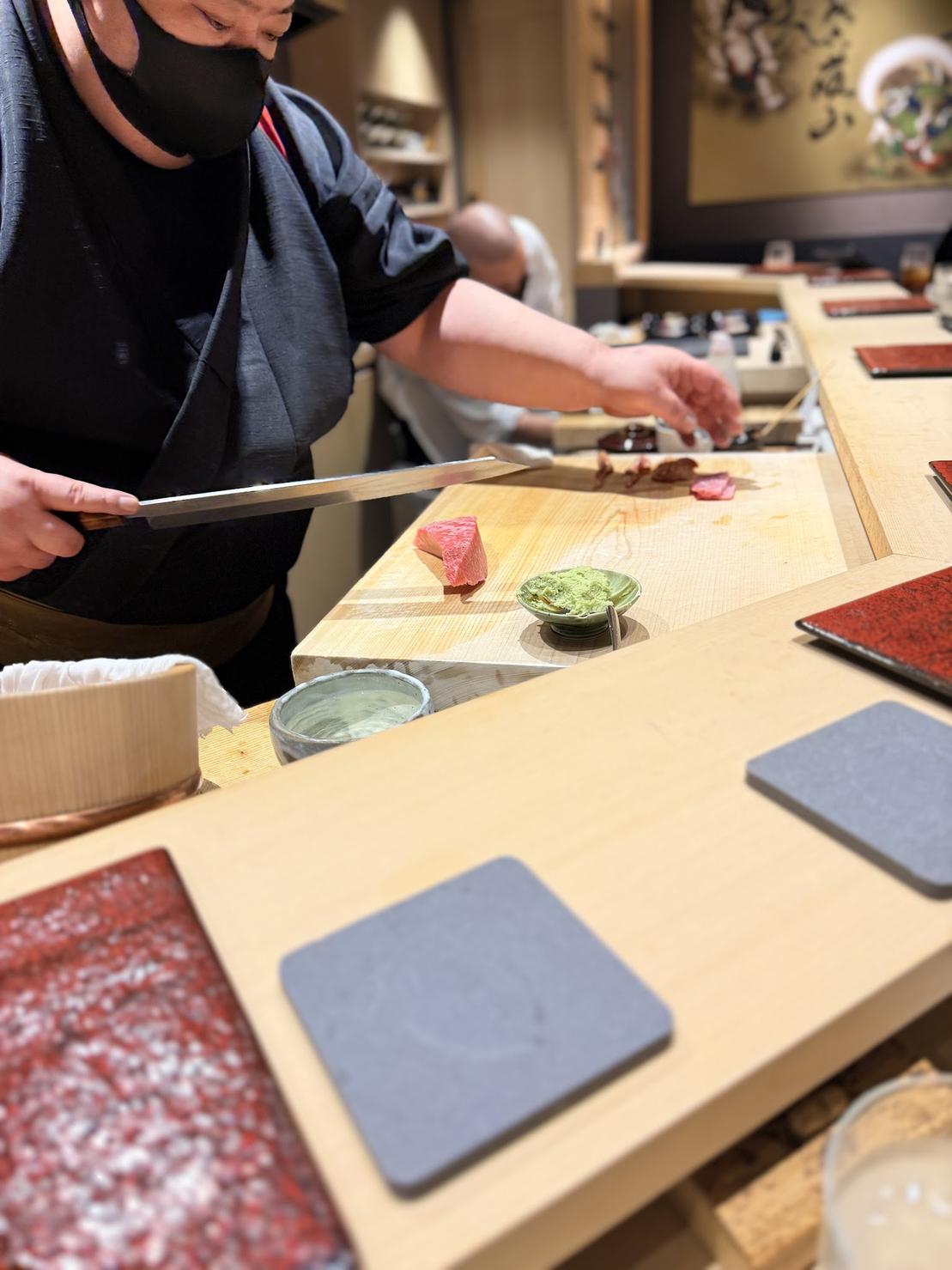 Sushi master slicing a block of tuna behind the cypress counter