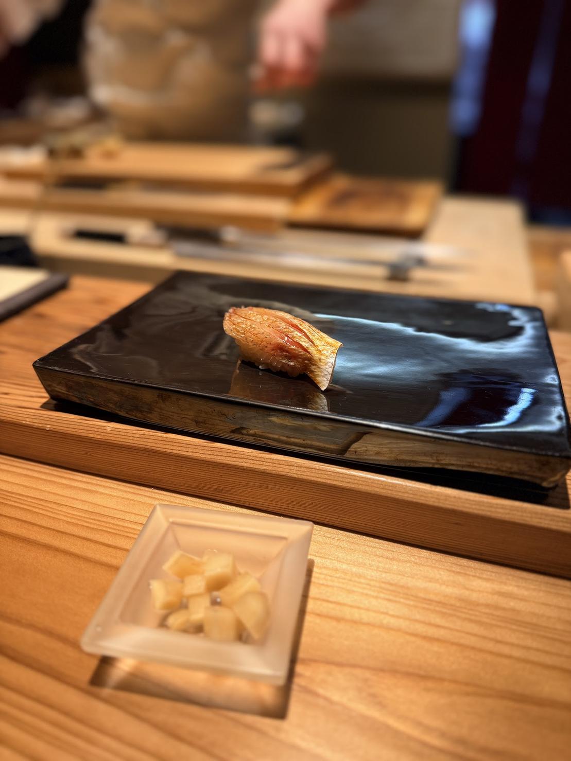 A piece of lightly torched nigiri resting on a glossy black plate at Karin sushi in Ryogoku