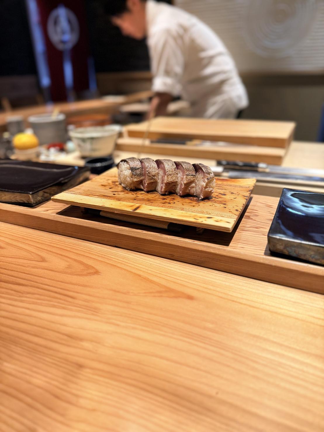 A nori-wrapped bite of marinated tuna held in hand over a small cup