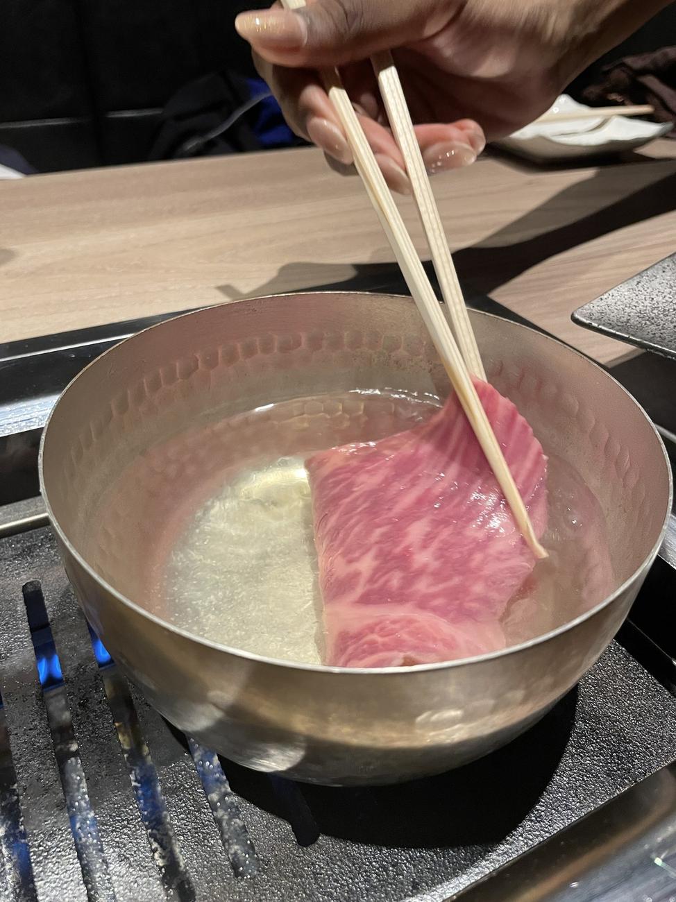 Thin slice of wagyu beef being dipped into hot broth for shabu-shabu