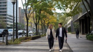 Two travelers in light autumn layers walking along a tree-lined avenue in central Tokyo in October