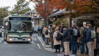 Travelers beside a busy Kyoto bus stop during the autumn season