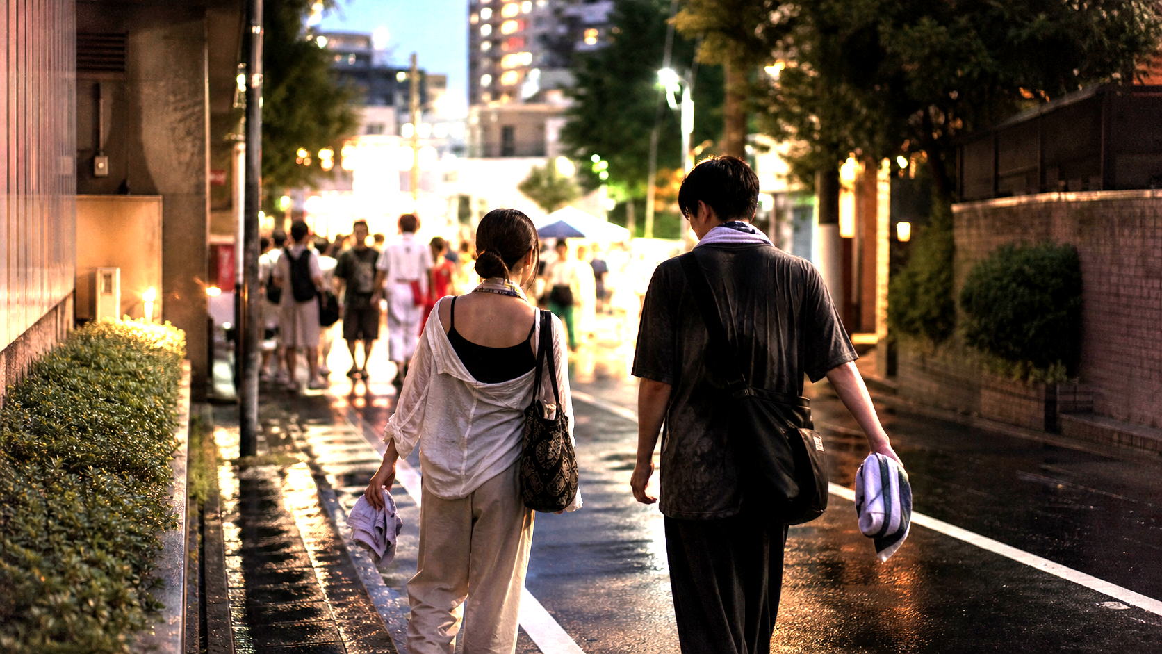 Travelers leaving a wet Tokyo festival street at dusk.