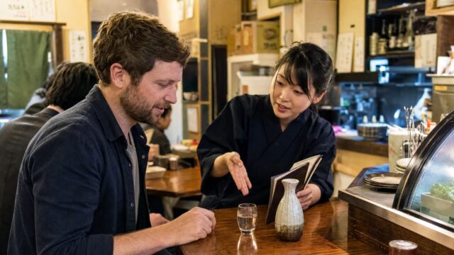 Traveler asking a restaurant server for a sake recommendation at a Tokyo izakaya counter