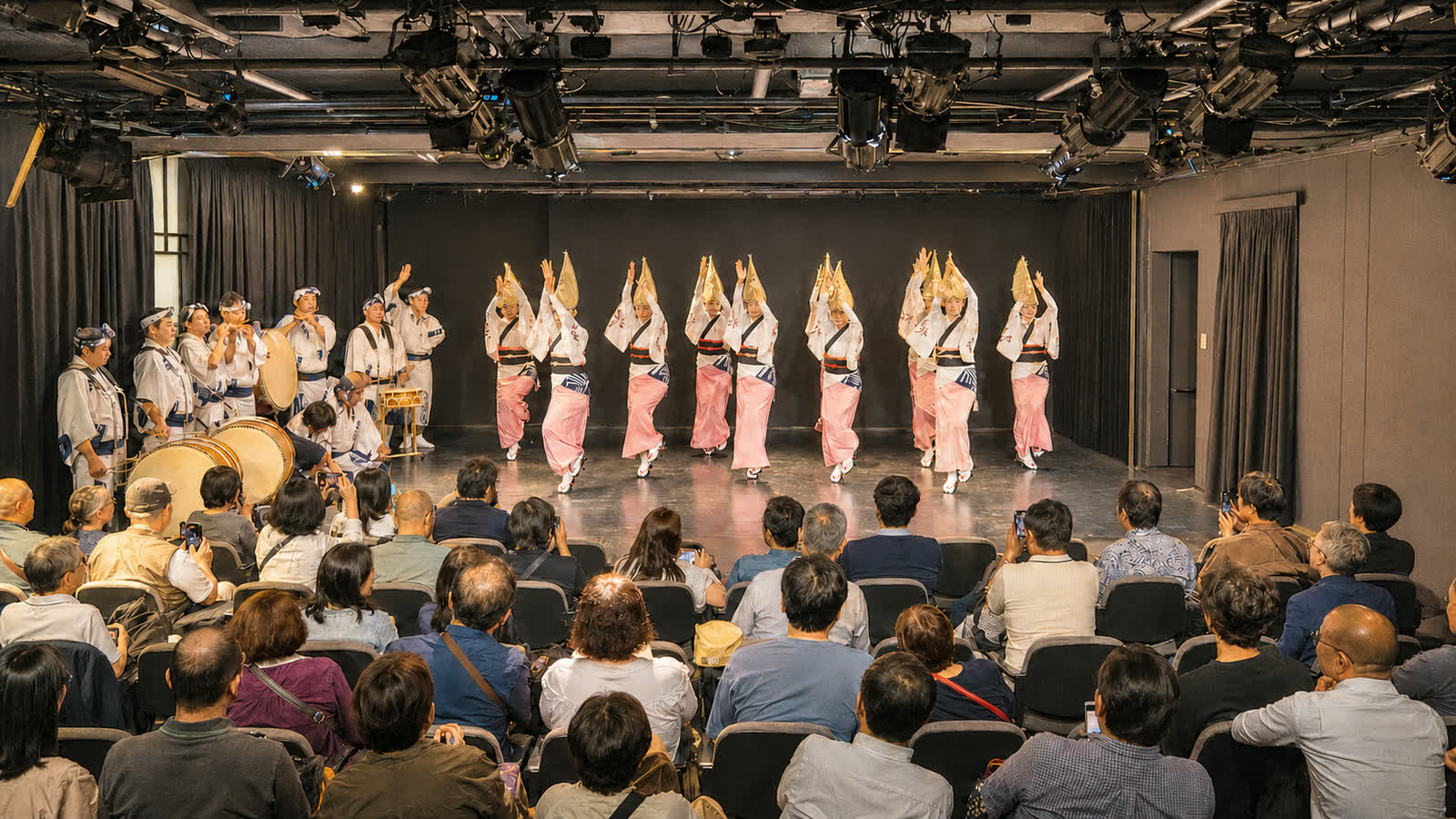 An indoor daytime Awa Odori stage performance with seated spectators