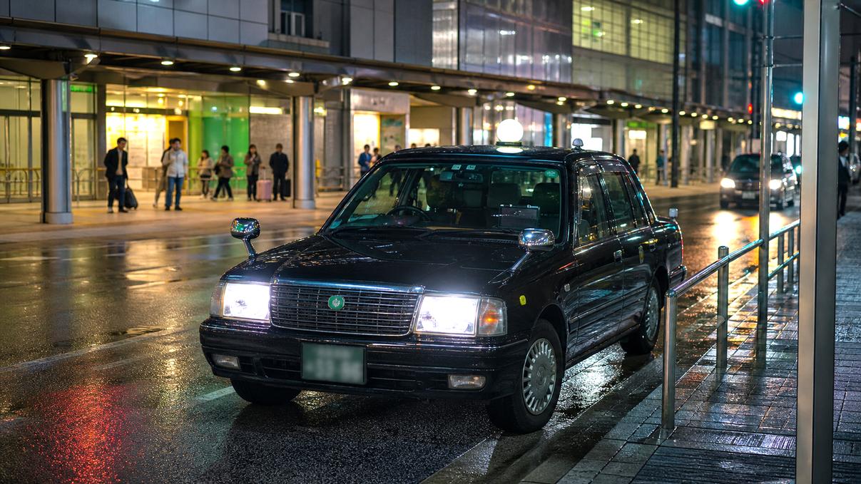 Licensed Tokyo taxi waiting near a station taxi stand on a wet late-night street.