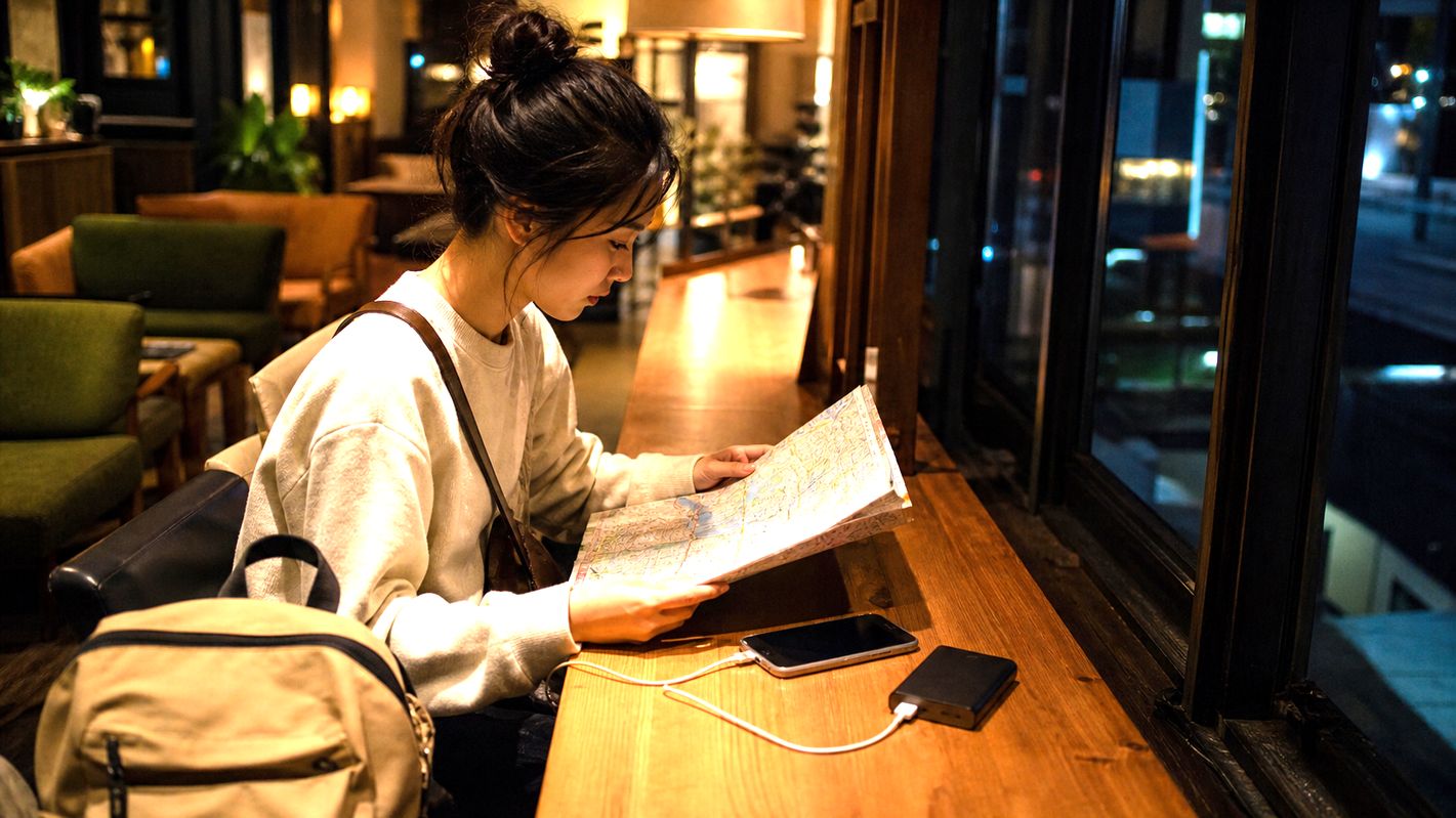 Traveler waiting indoors with a phone and map while planning the first train route.