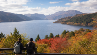 Two travelers overlooking Lake Ashi and autumn-colored mountains in Hakone