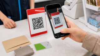 Visitor scanning a generic QR payment placard at a Japanese checkout with yen and an IC card ready as backups