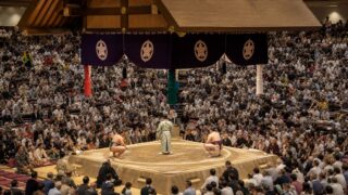 A sumo ring under arena lights with spectators seated around the dohyo