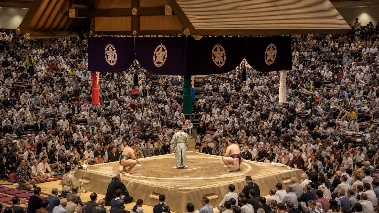 A sumo ring under arena lights with spectators seated around the dohyo