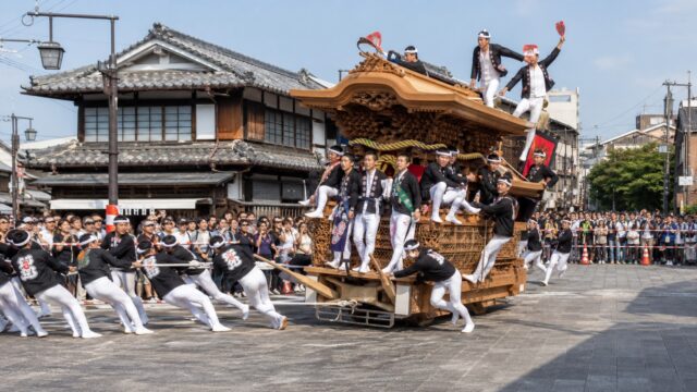 A carved Kishiwada danjiri turning through a traditional street as spectators watch from behind a safety line