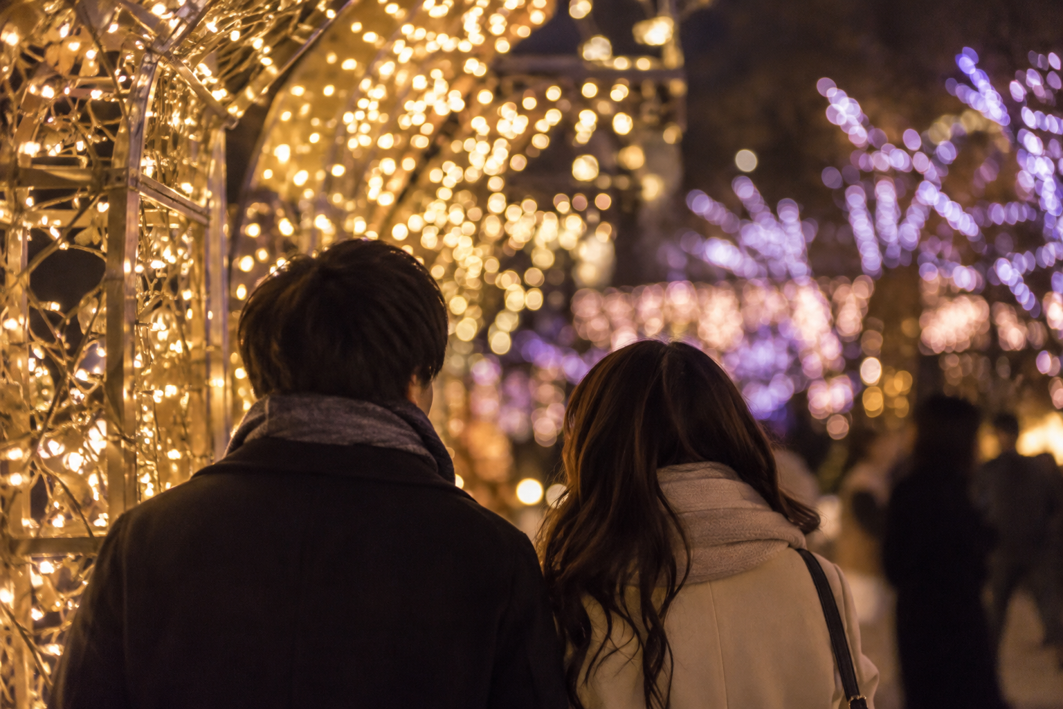 Two visitors in coats looking toward generic golden and violet lights
